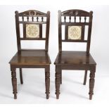A pair of aesthetic movement oak hall chairs with floral tile set to the spindle backs,