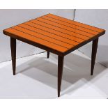Mid Century occasional table, having a square top with orange reserves and rising on tapered legs,