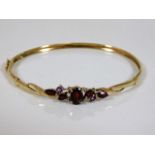 A 9ct gold bangle set with garnet, pearl & four sm