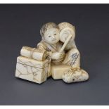 Small Japanese carved ivory okimono, Meiji period, depicting a seated boy with boxes and a scroll