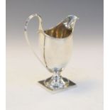 George III silver helmet shaped cream jug having a high loop handle and standing on a square foot,