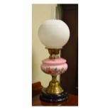 Victorian oil lamp having a pink glass reservoir with painted floral decoration, brass bell shaped