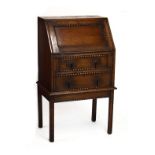 Early 20th Century oak bureau of narrow proportions with sloping fall over two drawers on stand