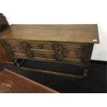 An oak Lincolnshire Dresser base with carved doors and drawers resting on turned legs.