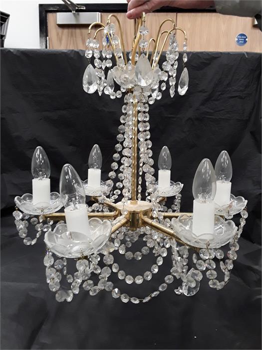 A brass six branch chandelier with cut glass droplets and six glass cups.