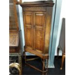 A carved oak corner cupboard on legs.