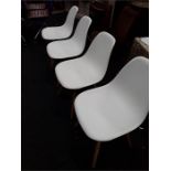 Four mid 20th century styled white plastic dining chairs with wooden legs.