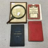 A brass magnifying glass with a selection of books and maps.