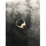 A gold ring with large red stone and white stone surround.
