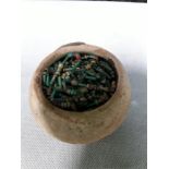 A collection of Egyptian pottery beads of various colours in a clay pot.