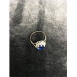 A gold ring with large blue stone and white stone surround.
