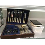 A cutlery canteen together with another tub of cutlery.