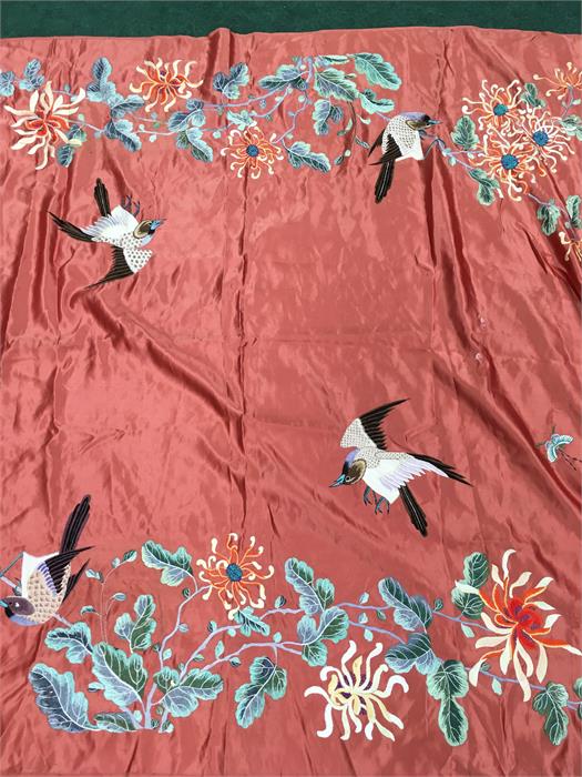 A Chinese coral pink coloured silk panel embroidered with birds and flowers.