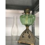 An oil lamp on a brass base with green glass reservoir and funnel.