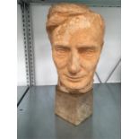 A terracotta sculpture of a gentleman’s head mounted on a wooden plinth.