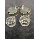 A pair of silver mustard pots with lids together with a pair of cut glass salts with silver rims.