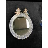 A Dresden oval mirror with porcelain frame encrusted with flowers and topped with two cherubs.(35cms