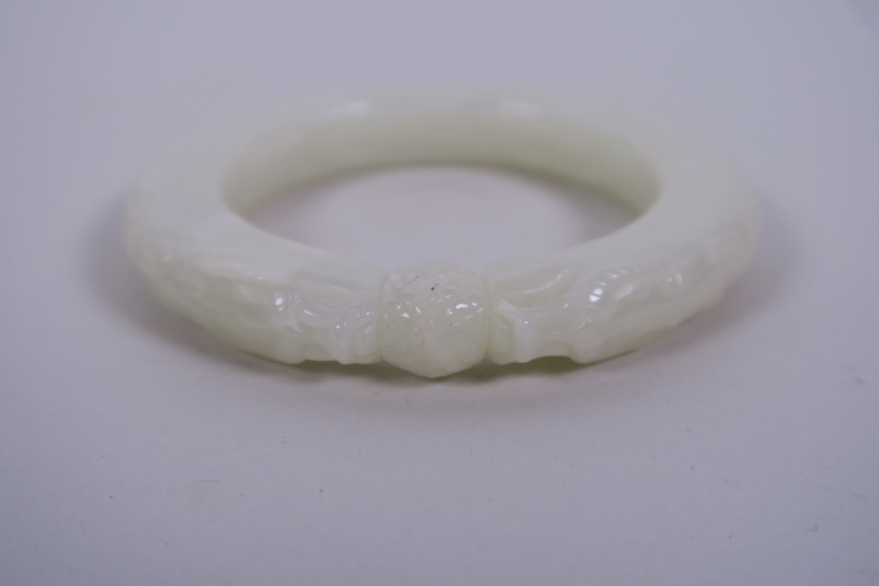 A Chinese carved white jade bangle with dragon head decoration, 3" diameter