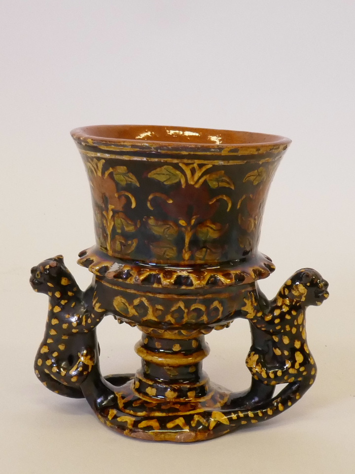 A slipware pottery goblet with polychrome floral decoration and leopard handles, 5" high