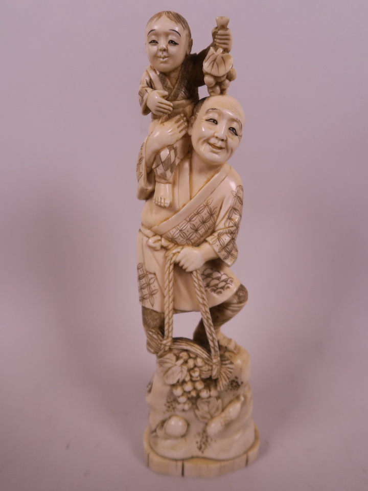 A Japanese carved marine ivory figurine of a farmer with a small child on his shoulder, a basket