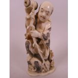 A Japanese carved ivory figurine of a sage holding a barrel and ragged staff, standing on a bag of
