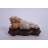 A Chinese carved jade ornament in the form of a kylin, mounted on a carved hardwood base, 5" long