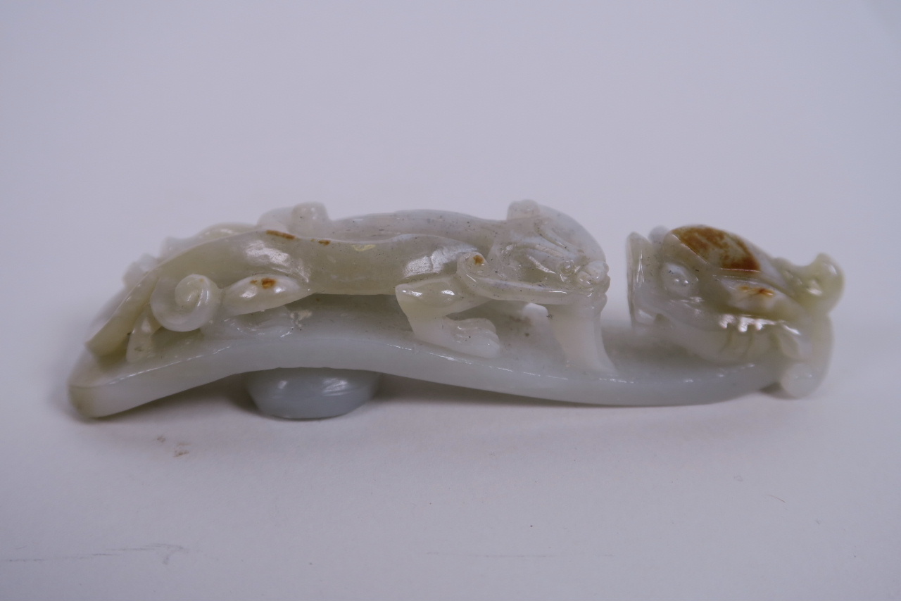 A Chinese celadon jade belt hook carved in the form of a dragon, 4½" long