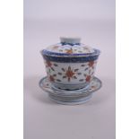 A Chinese blue and white rice grain porcelain tea bowl, lid and stand, with lotus flower decoration,