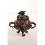 A Chinese two handled bronze censer and cover on tripod paw feet, with dragon and mask decoration,