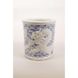 A Chinese blue and white porcelain brush pot with raised decoration of a dragon catching carp,