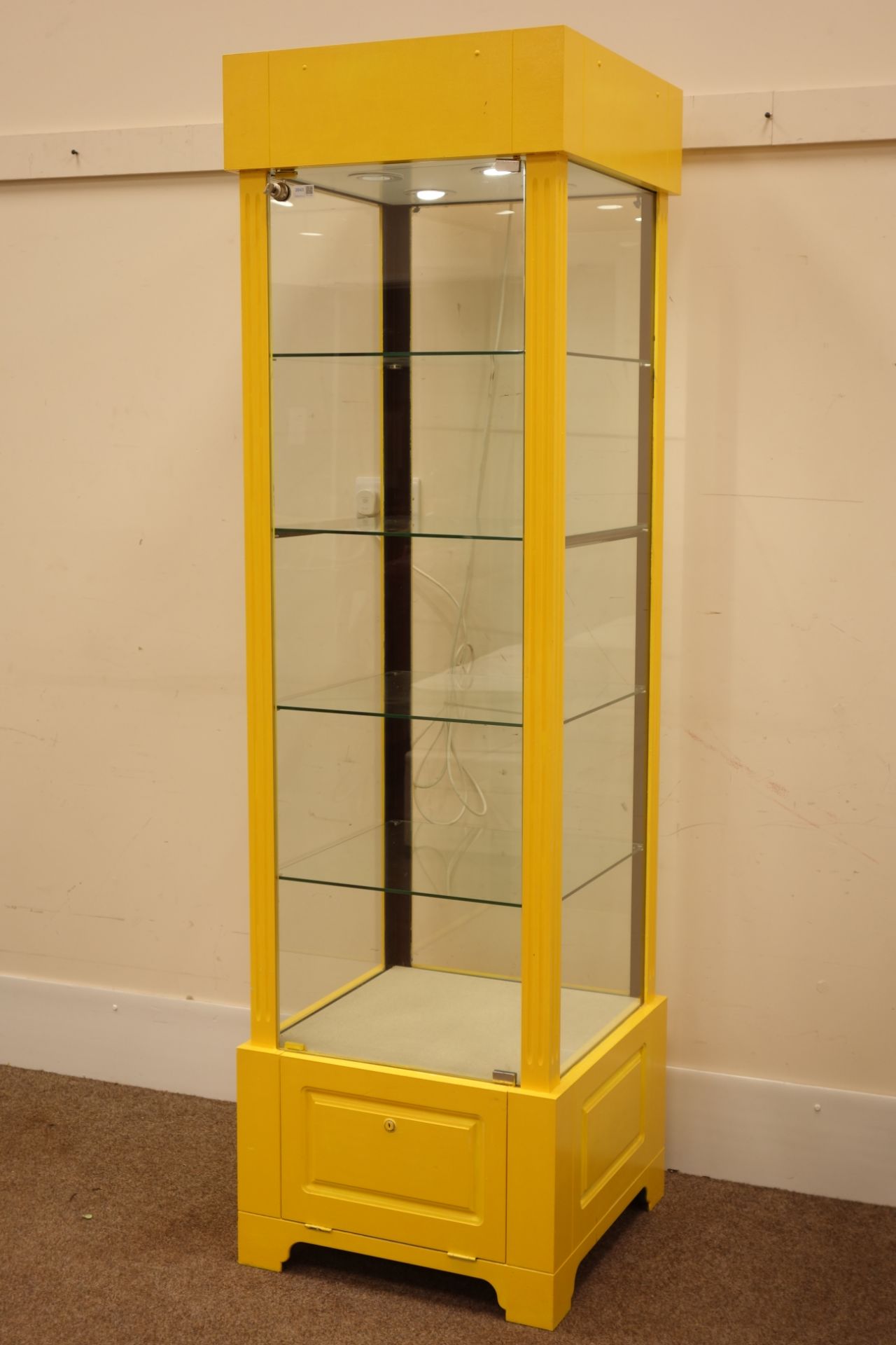 Tall narrow four sided glass shops display cabinet, illuminated interior,