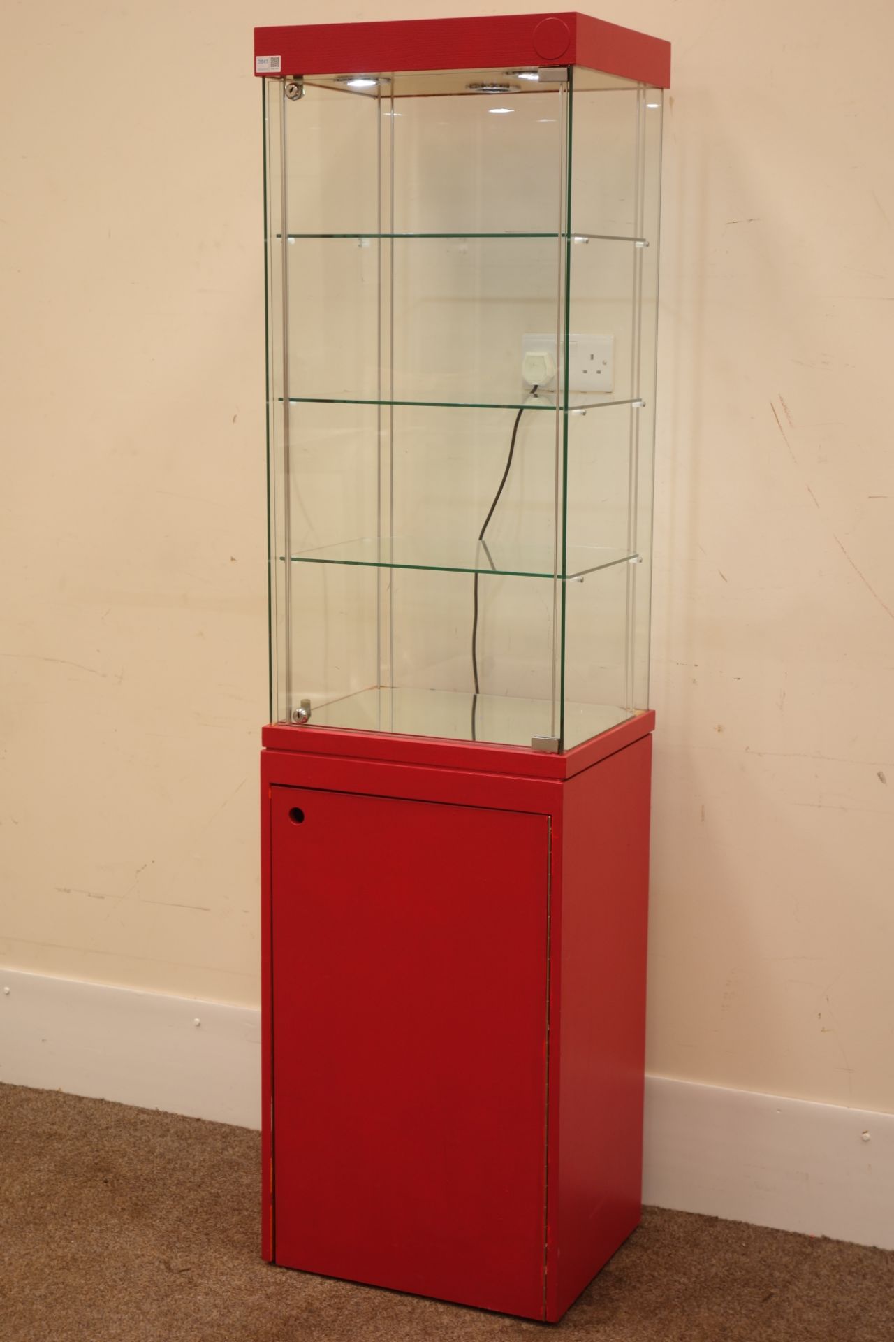 Tall narrow four sided glass shops display cabinet, illuminated interior, cupboard below.