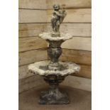 Composite stone water feature, cherub holding fish spout above two circular scalloped shell tiers,