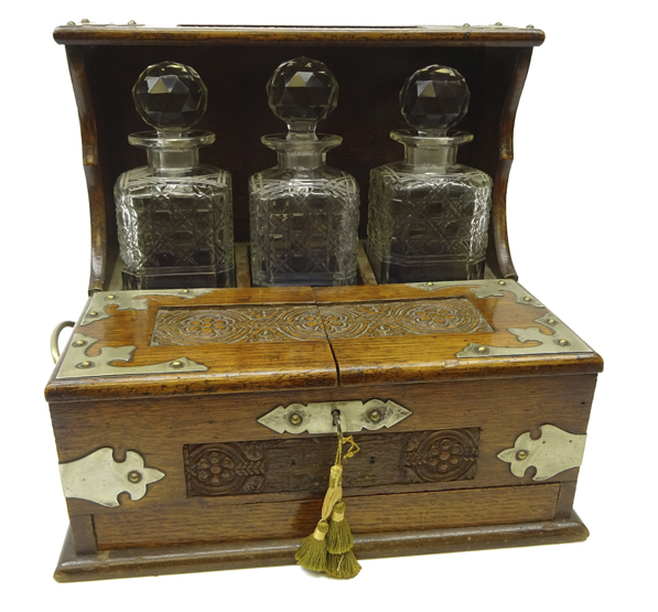 Edwardian oak three bottle tantalus with silver-plated mounts, carved floral panels,