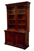 Victorian mahogany bookcase on cupboard, projecting cornice above two arched glazed doors,