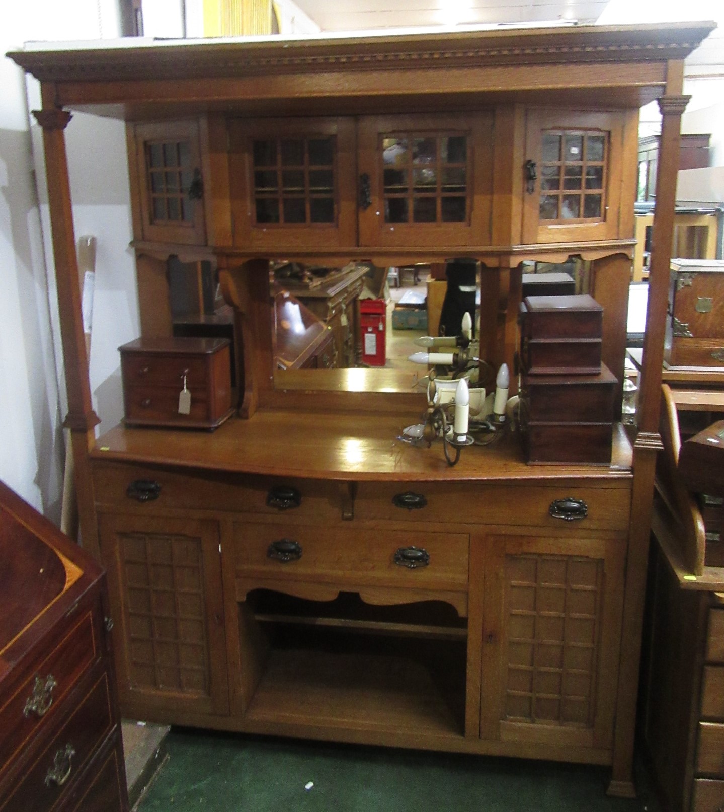 An Arts and Crafts light oak sideboard, the four glazed cupboard doors above three mirrored plates,