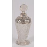 An Edwardian cut glass toilet bottle with embossed silver mounted shoulder and faceted stopper,