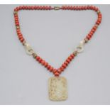 A Chinese carved jade pendant hanging from a red coral bead necklace with jade rings and filigree