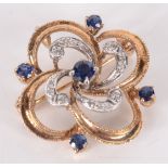 A yellow and white gold swirl brooch set with diamonds and sapphires.