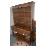 A carved oak dresser, 20th century, the scroll and leaf decorated apron above three shelves,