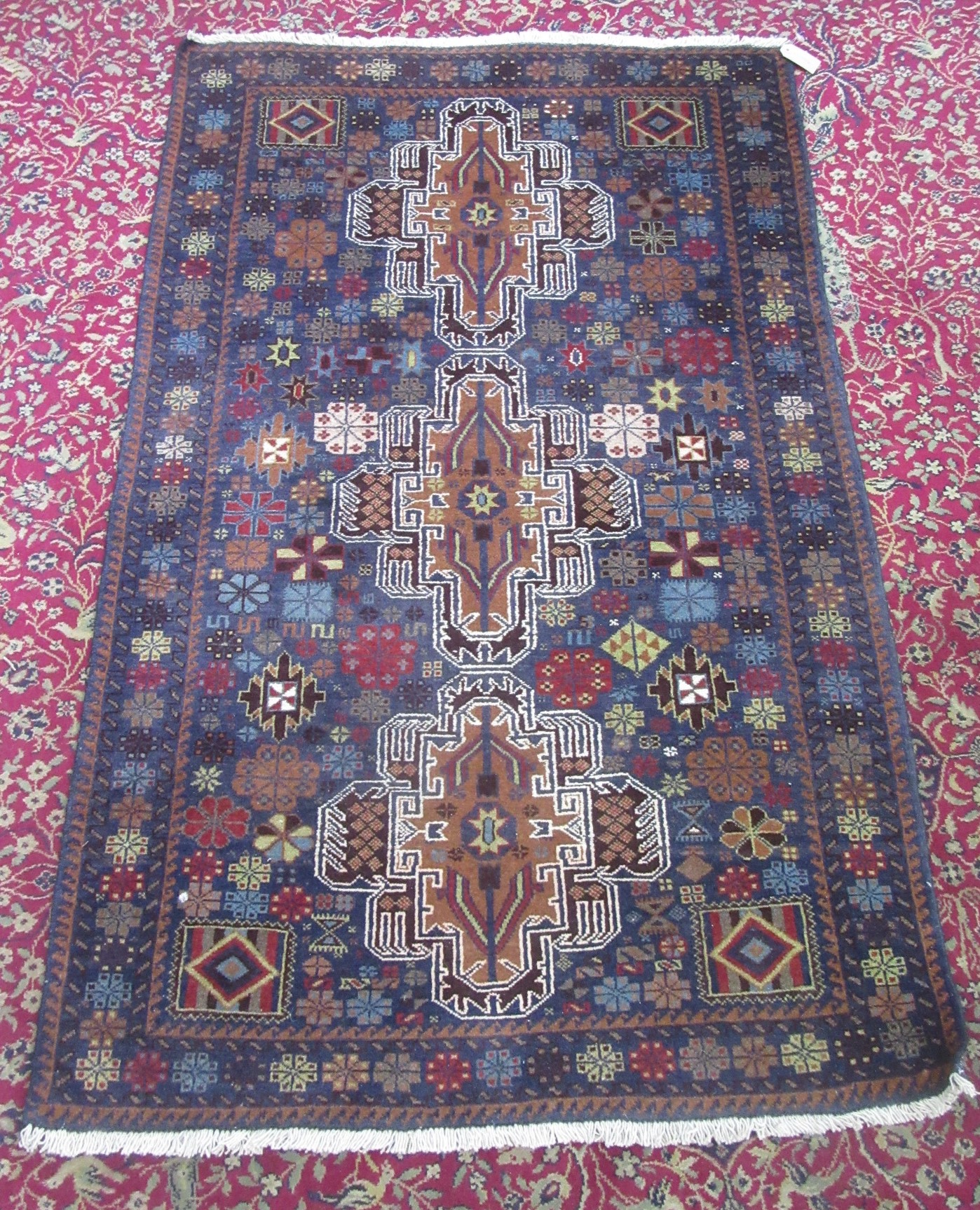 An Afghan Belouch rug, the indigo field with three brown lobed medallions,