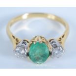 An 18ct gold ring set an emerald flanked by diamonds.