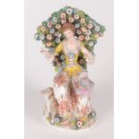 A continental porcelain figure of a lady, circa 1900, she sits before a flowering tree,