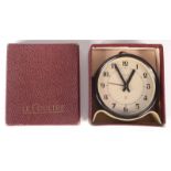 A Le Coultre alarm clock, circa 1930s, in a black circular case on a cream shaped stand,