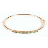 A 9ct gold bangle, set with eight emeralds and seven diamonds, boxed.