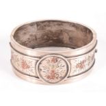 A late Victorian Aesthetic movement silver bangle with applied two colour gold decoration.