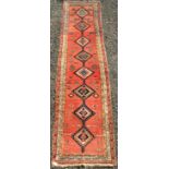 A North West Persian runner, the madder field with eight linked polychrome medallions, people,