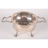 A twin handled silver tea strainer in 18th century style with stand on three shell capped legs,