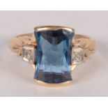 An American gold ring set a fancy cut blue stone between diamonds.
