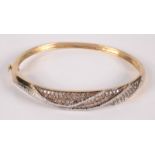 A gold bangle pave set with three serpentine lines of white diamonds on a ground of champagne